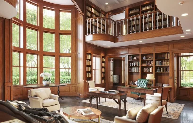 A wood-paneled library office with floor-to-ceiling bookshelves, tall windows, and an executive desk with a green leather chair